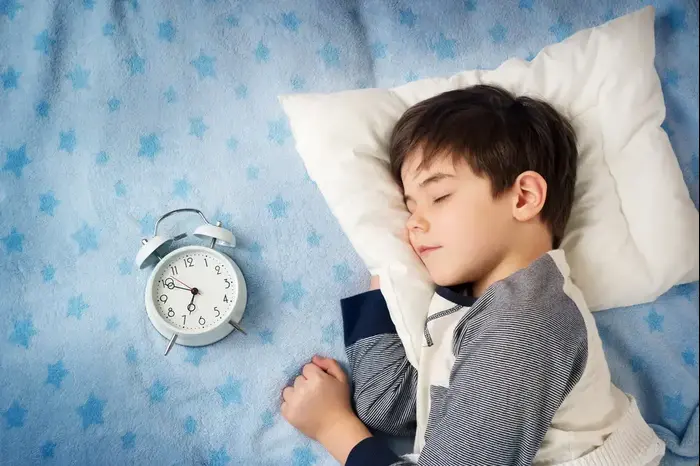 ילד ישן במיטה לצד שעון מעורר (ShutterStock) ילד ישן במיטה לצד שעון מעורר (ShutterStock)