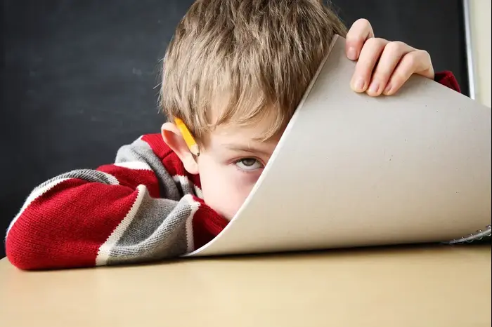ילד מסתתר מאחורי מחברת בכיתה (ShutterStock) ילד מסתתר מאחורי מחברת בכיתה (ShutterStock)