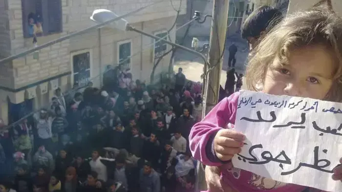 ילדה נושאת שלט שעליו נכתב "רוצים אזור אסור לטיס" בהפגנה נגד שלטונות סוריה בעיר חומס, 27 בדצמבר 2011 ילדה נושאת שלט שעליו נכתב "רוצים אזור אסור לטיס" בהפגנה נגד שלטונות סוריה בעיר חומס, 27 בדצמבר 2011