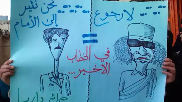 שלט "אסד = קדאפי" בהפגנה נגד שלטונות סוריה בעיירה דאריה, פרבר של דמשק, 14 הינואר 2011 שלט "אסד = קדאפי" בהפגנה נגד שלטונות סוריה בעיירה דאריה, פרבר של דמשק, 14 הינואר 2011