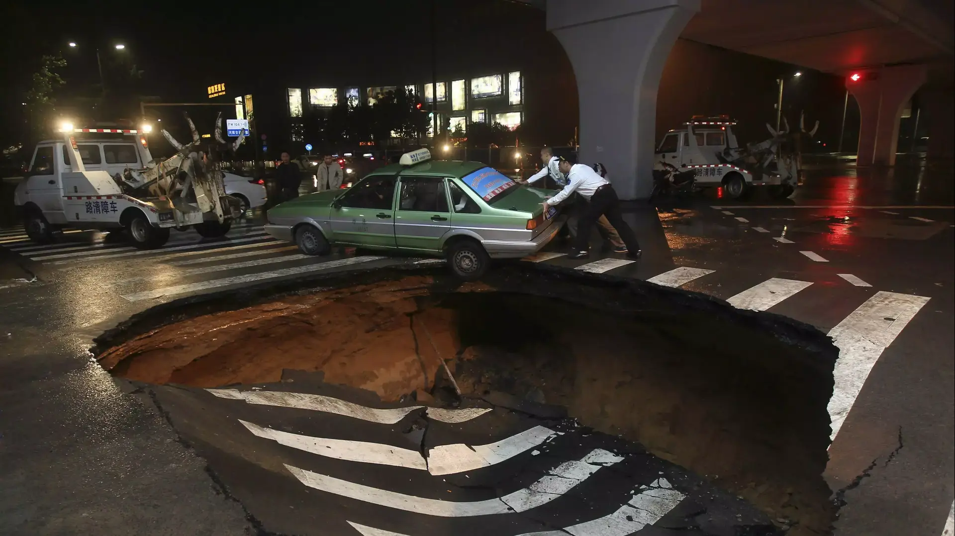 אנשים מנסים לדחוף מונית תקועה בכביש ששקע כתוצאה מסופות במחוז הנאן, סין אנשים מנסים לדחוף מונית תקועה בכביש ששקע כתוצאה מסופות במחוז הנאן, סין