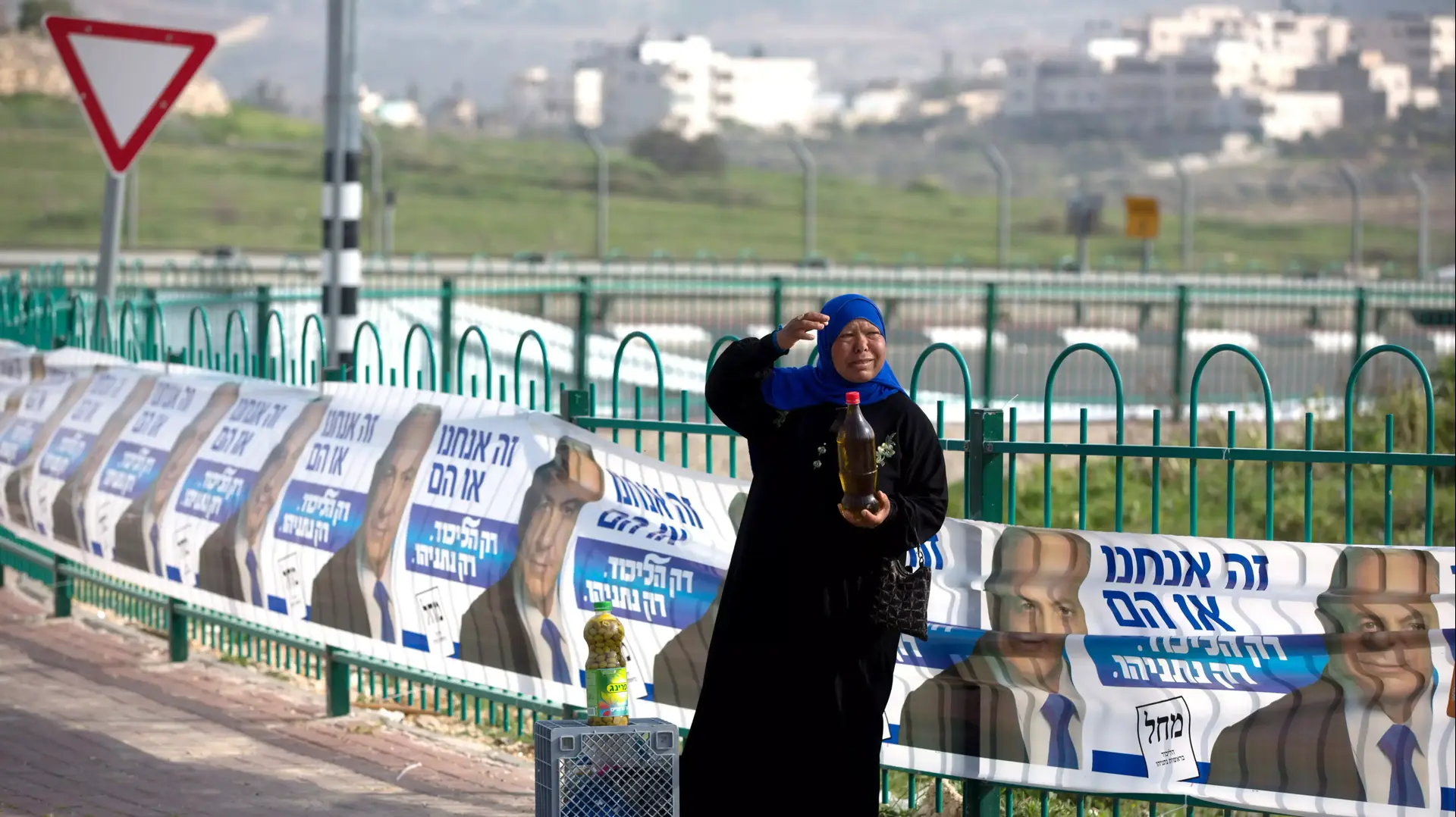 אישה פלסטינית מוכרת שמן זית ליד שלטי בחירות של הליכוד באזור גבעת זאב, מרץ 2015 אישה פלסטינית מוכרת שמן זית ליד שלטי בחירות של הליכוד באזור גבעת זאב, מרץ 2015