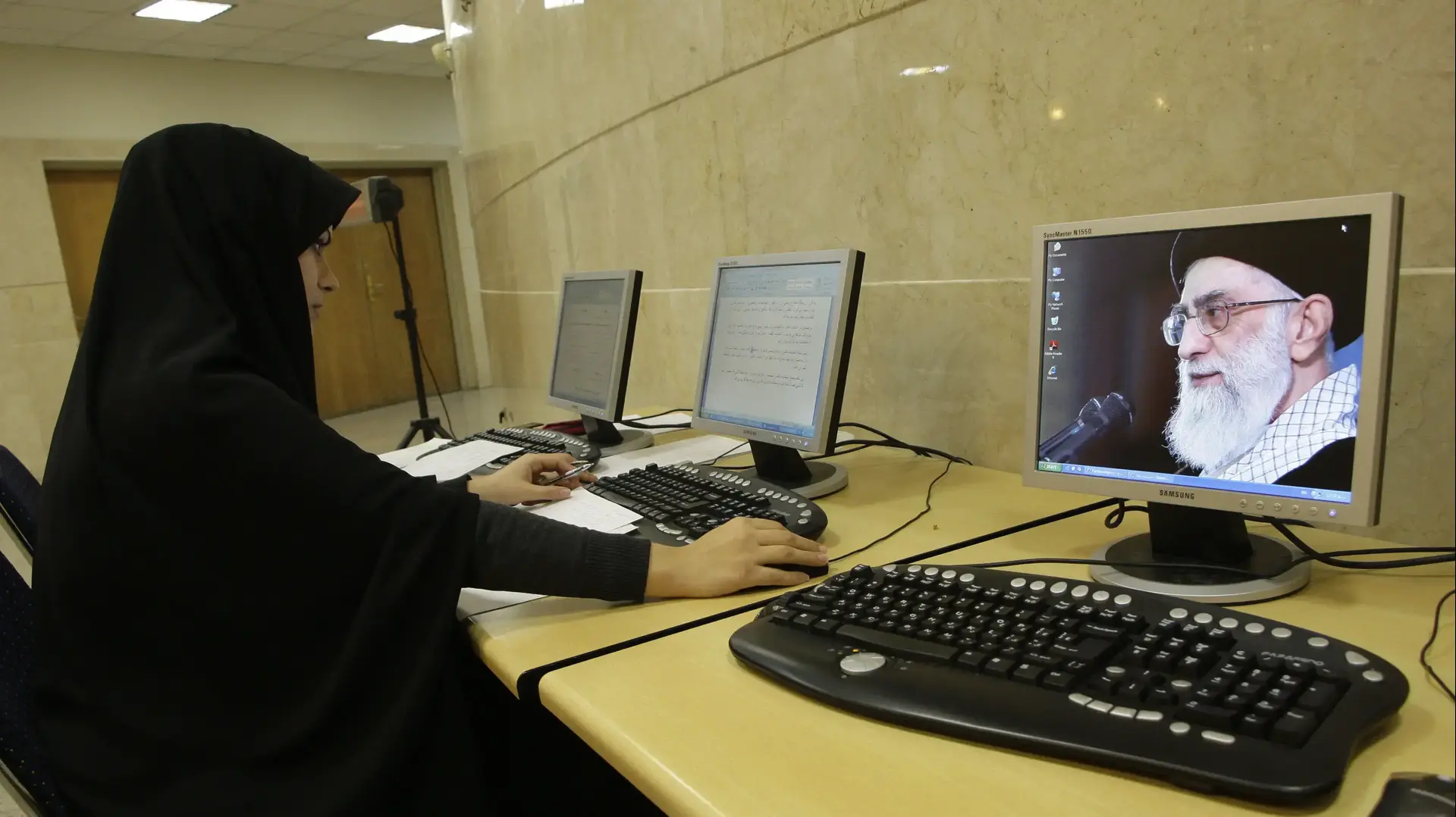 אישה באיראן משתמשת במחשב ולצדה תמונה של המנהיג העליון עלי חמינאי