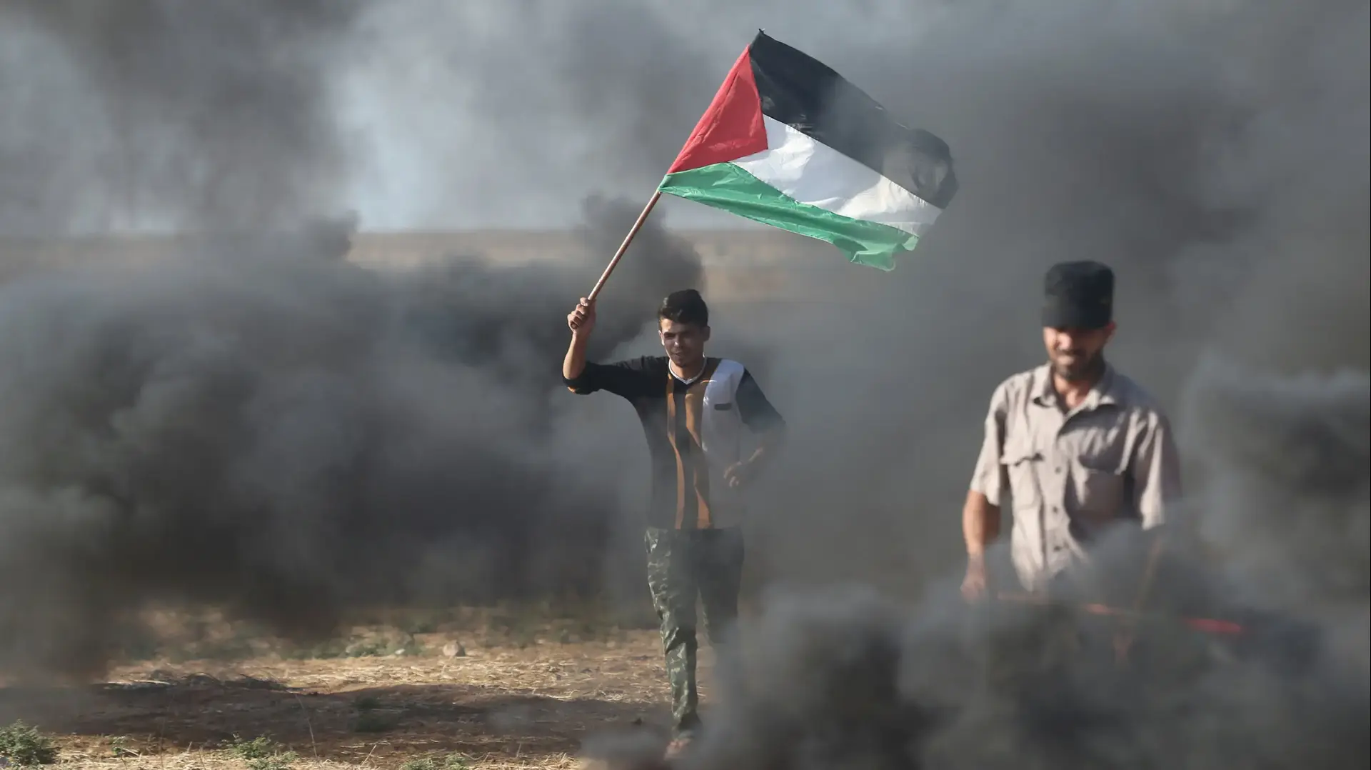 מפגין פלסטיני מחזיק בדגל פלסטין במהלך עימותים עם כוחות ישראליים במחאה על צמצום אספקת החשמל לעזה, סמוך לח'אן יונס, דרום הרצועה מפגין פלסטיני מחזיק בדגל פלסטין במהלך עימותים עם כוחות ישראליים במחאה על צמצום אספקת החשמל לעזה, סמוך לח'אן יונס, דרום הרצועה
