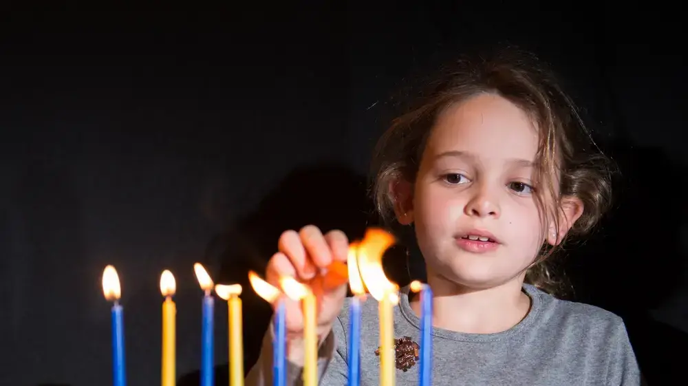 ילדה מדליקה נרות חנוכה בחנוכיה - חנוכה 2023 ילדה מדליקה נרות חנוכה בחנוכיה - חנוכה 2023