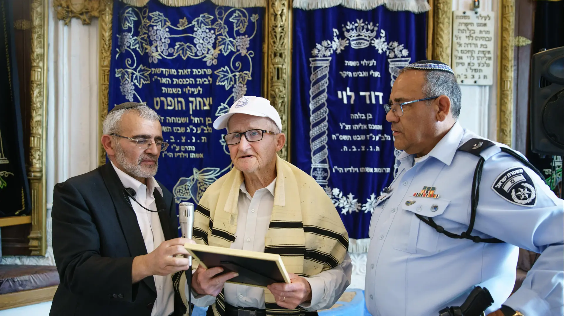 חנוך שחר חגג בר מצוה בגיל 83 כדי להזכיר את סיפורם של הילדים בשואה, מימינו, השוטר ירון המאירי שנתן לו תעודת הערכה על ההתנדבות במשטרה, משמאלו שלמה חדד שלימד אותו את ההפטרה 8 במרץ 2018