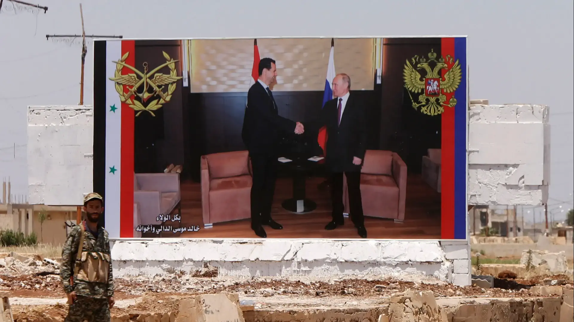 חייל סורי עומד מול שלט חוצות של אסד עם פוטין בכביש המחבר חומס לחמאת, 6 ביוני 2018 חייל סורי עומד מול שלט חוצות של אסד עם פוטין בכביש המחבר חומס לחמאת, 6 ביוני 2018