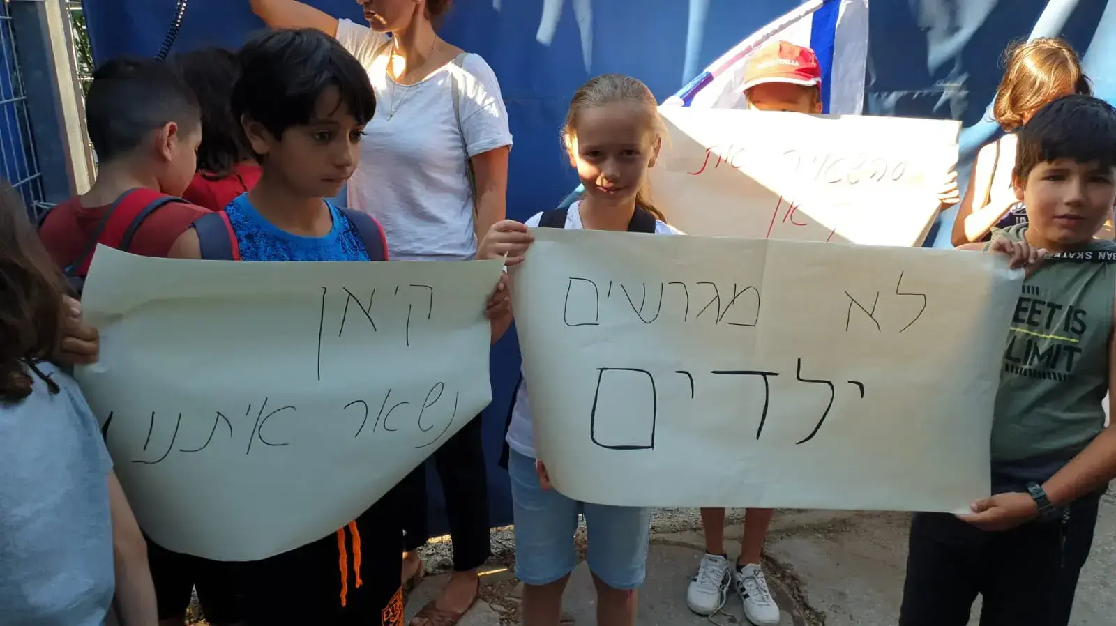 חבריהם לכיתה של ילדיה של ג'רלדין מפגינים יחד עם הוריהם מול הכניסה למתקן המשמורת נגד הגירוש, נתב"ג