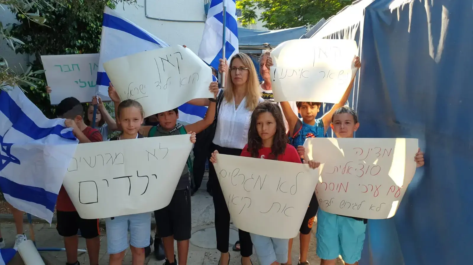 חבריהם לכיתה של ילדיה של ג'רלדין מפגינים יחד עם הוריהם מול הכניסה למתקן המשמורת נגד הגירוש, נתב"ג