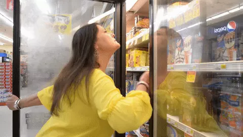 אישה בגל חום מקררת את הפנים שלה מול מקרר בסופר אישה בגל חום מקררת את הפנים שלה מול מקרר בסופר