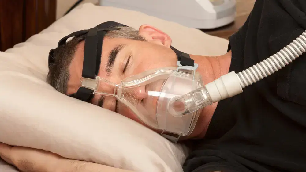 גבר ישן במיטה מחובר למכשיר CPAP להקלה על דום נשימה בשינה גבר ישן במיטה מחובר למכשיר CPAP להקלה על דום נשימה בשינה