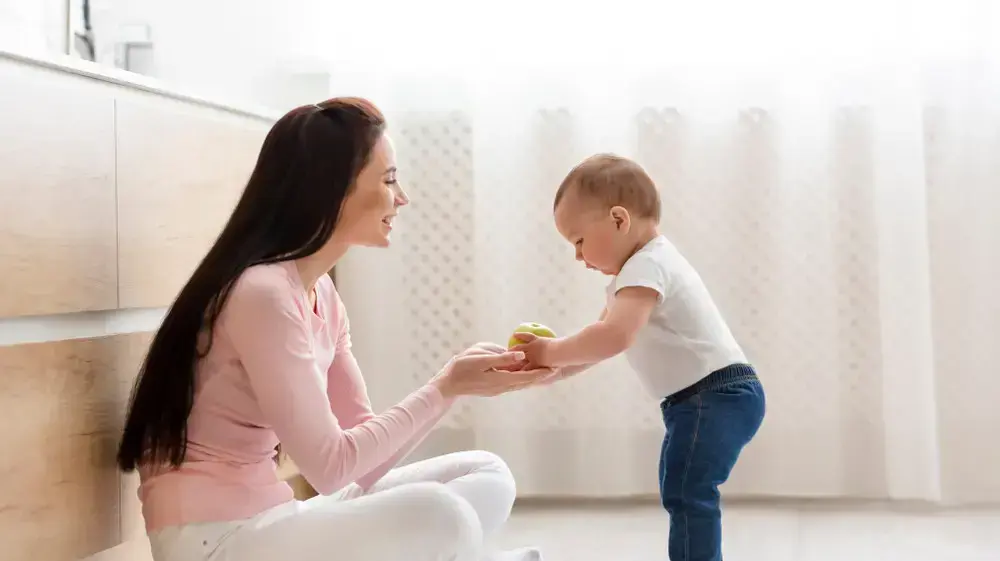 תינוק עומד מניח תפוח בידיים של אמא שלו תינוק עומד מניח תפוח בידיים של אמא שלו
