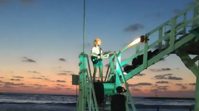 מיקה שדה מופיעה על סוכת מציל בחוף פרשימן בתל אביב בימי משבר הקורונה, אוגוסט 2020 מיקה שדה מופיעה על סוכת מציל בחוף פרשימן בתל אביב בימי משבר הקורונה, אוגוסט 2020
