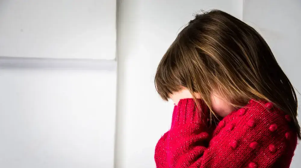 ילדה עצובה מליטה את פניה בין ידיה