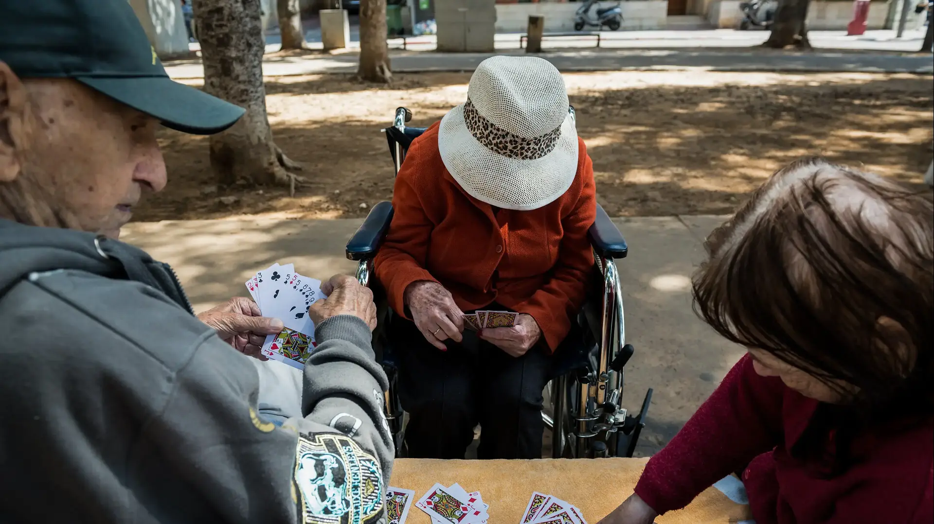 קשישים משחקים קלפים בספסל בשדרות 