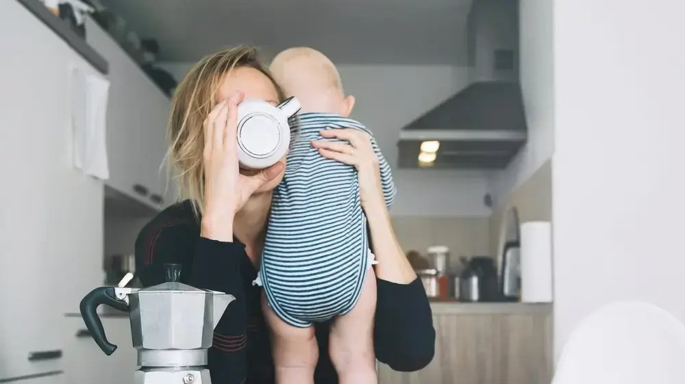 אמא עייפה שותה קפה ומחזיקה תינוק אמא עייפה שותה קפה ומחזיקה תינוק