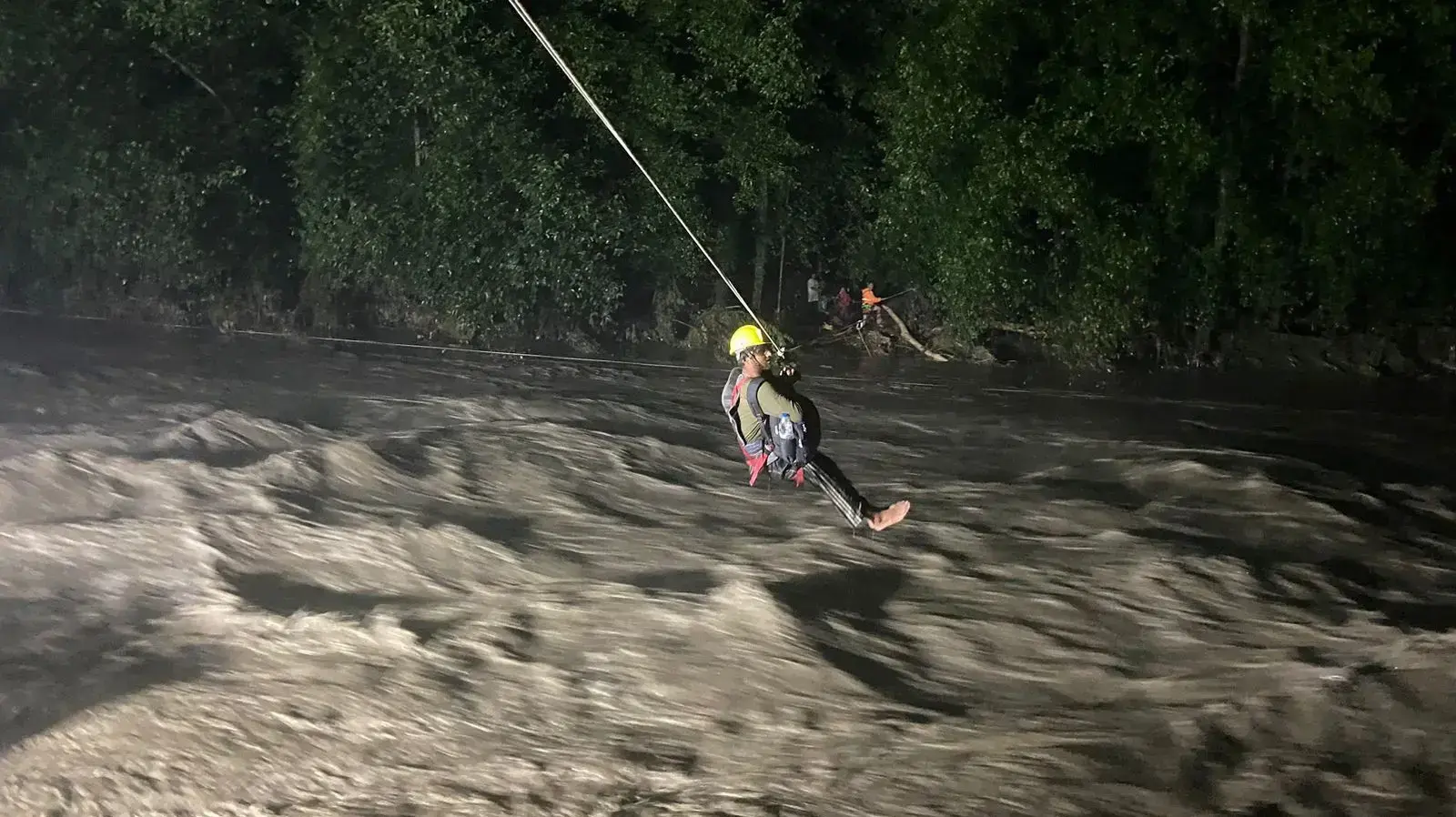 אדם עם רתמת בטיחות חוצה נהר שעלה על גדותיו בשל גשמי מונסון במדינת הימאצ'ל פרדש, הודו, 9 ביולי 2023