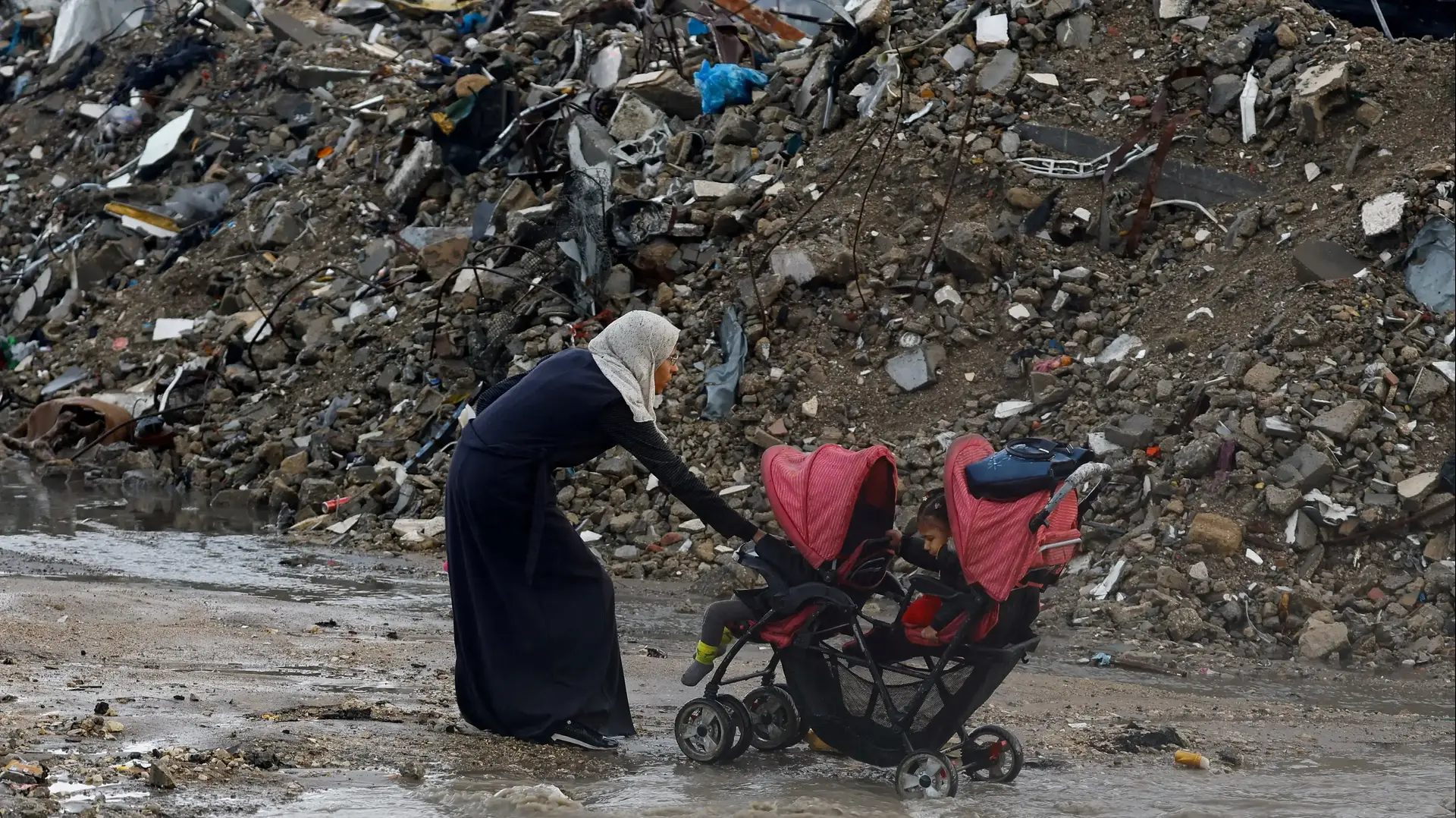 אישה עם עגלה בבוץ בעיר עזה, 25 בנובמבר 2025 אישה עם עגלה בבוץ בעיר עזה, 25 בנובמבר 2025