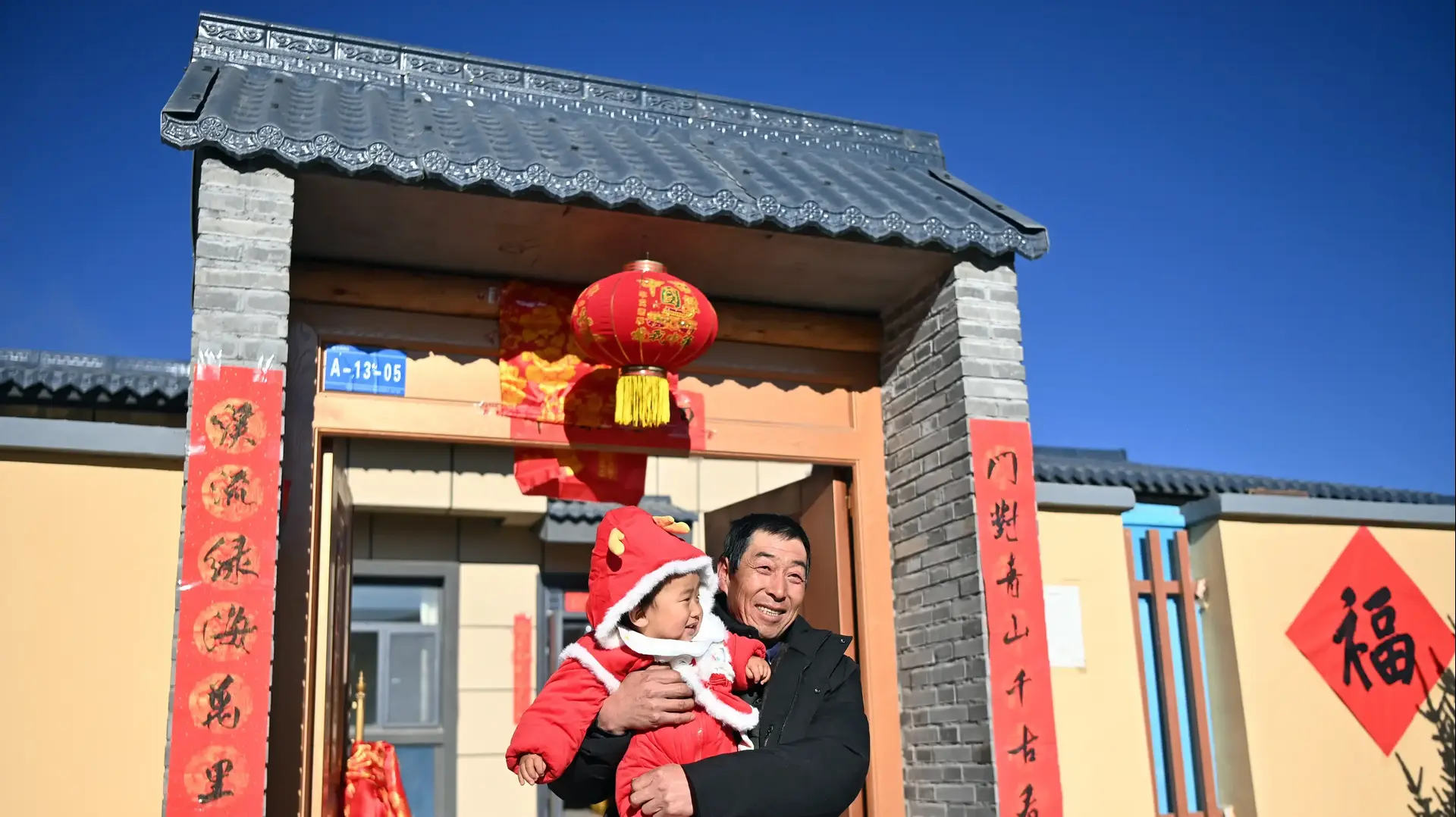 A villager carry a baby stands in front of the resettlement site on December 29, 2025 in Lanzhou, Gansu Province of China
