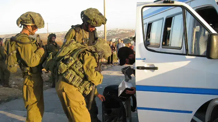 נהג הסעות פלסטיני מציג בפני חיילים במחסום את תיקיהם של הנוסעים לבדיקה