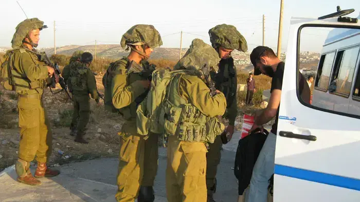 נהג הסעות פלסטיני מציג בפני חיילים במחסום את תיקיהם של הנוסעים לבדיקה