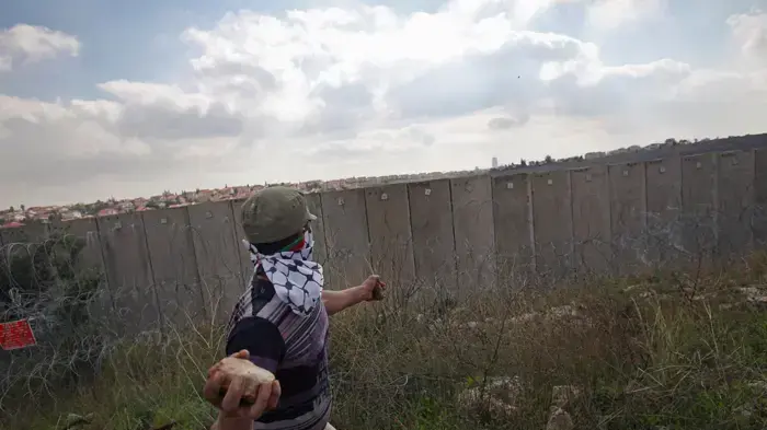 מפגין פלסטיני משליך אבן על כוח צה''ל בזמן הפגנה נגד בניית גדר ההפרדה בכפר ניעלין בשומרון