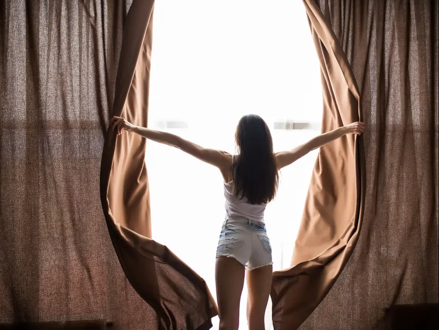 אישה פותחת וילון בבוקר. ShutterStock
