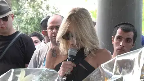 לירן חולצה אפורה נעמד מאחורי דפנה רכטר, בתה של חנה מרון, בעת שהספידה את אמה בהלווייה בקיבוץ שפיים לירן חולצה אפורה נעמד מאחורי דפנה רכטר, בתה של חנה מרון, בעת שהספידה את אמה בהלווייה בקיבוץ שפיים