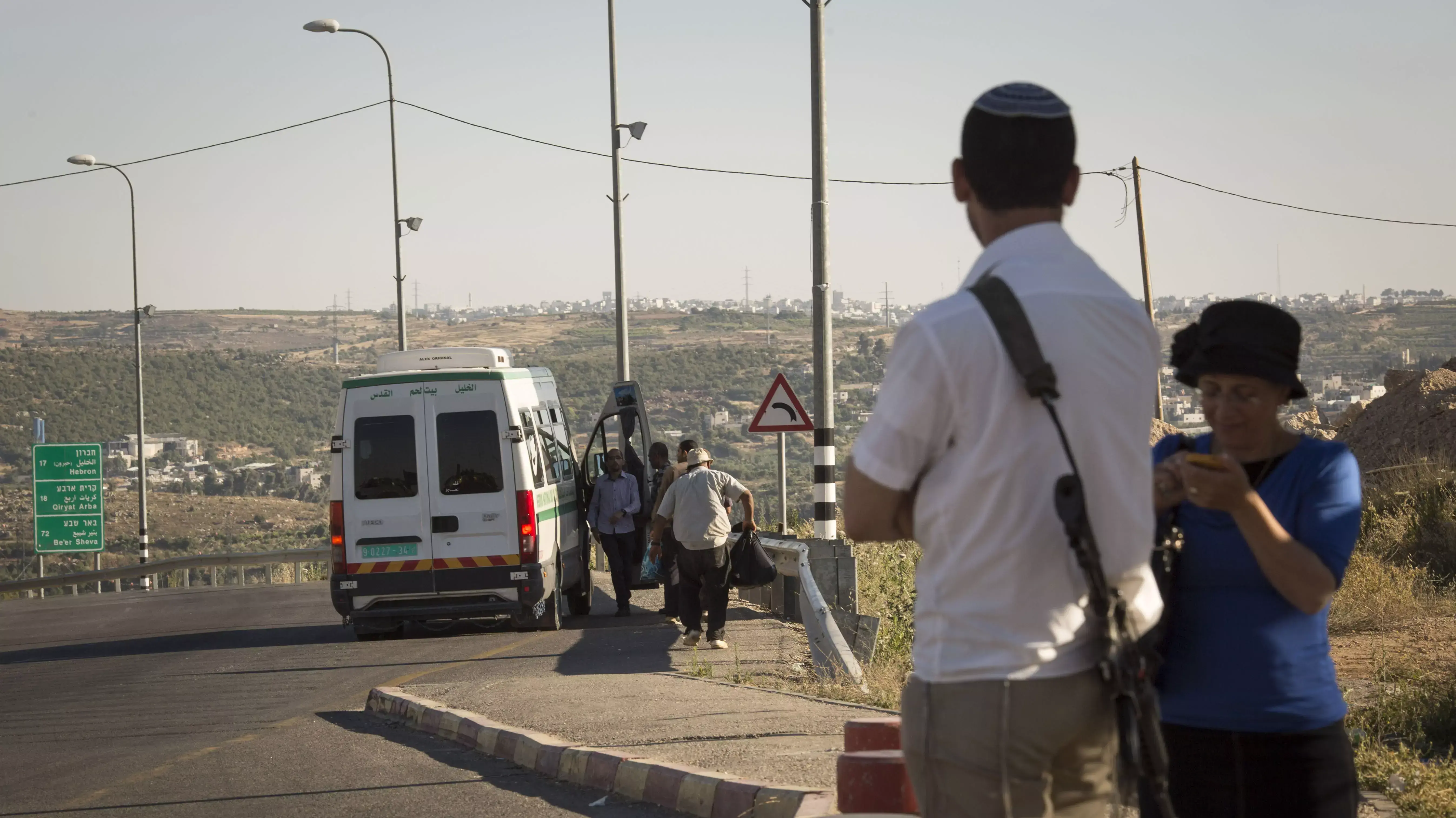 פלסטינים מחכים לצד הכביש במרחק מתחנת האוטובוס בצומת גוש עציון, בה עומדים מתנחלים פלסטינים מחכים לצד הכביש במרחק מתחנת האוטובוס בצומת גוש עציון, בה עומדים מתנחלים
