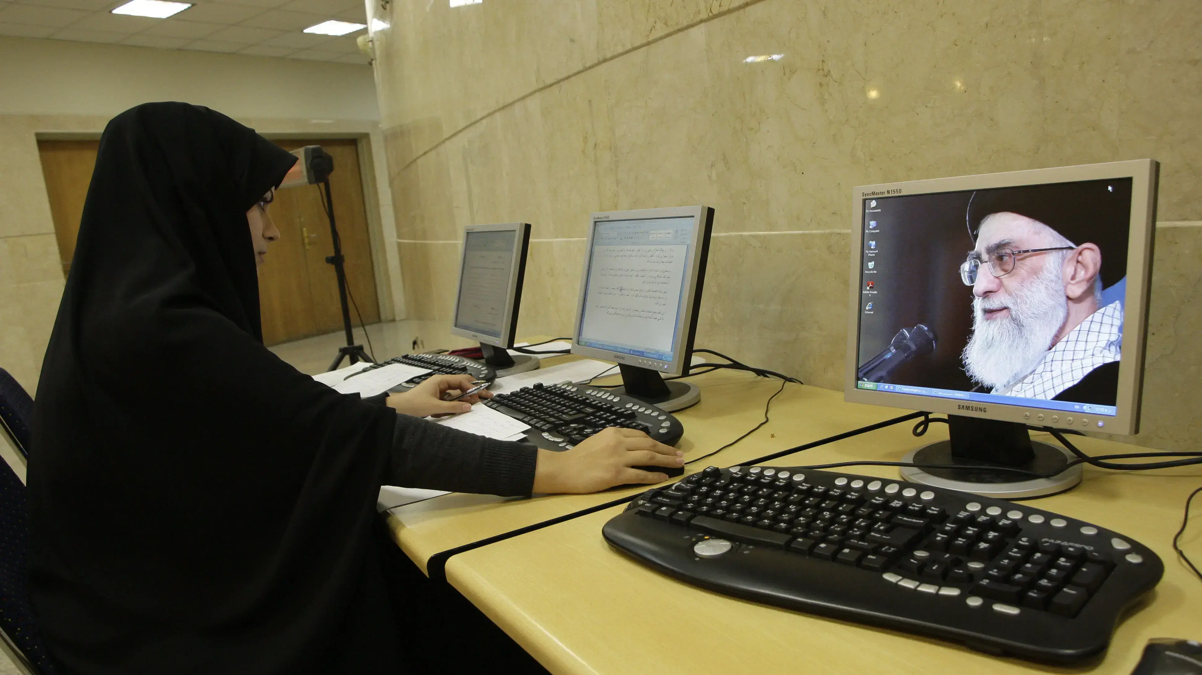 אישה באיראן משתמשת במחשב ולצדה תמונה של המנהיג העליון עלי חמינאי אישה באיראן משתמשת במחשב ולצדה תמונה של המנהיג העליון עלי חמינאי