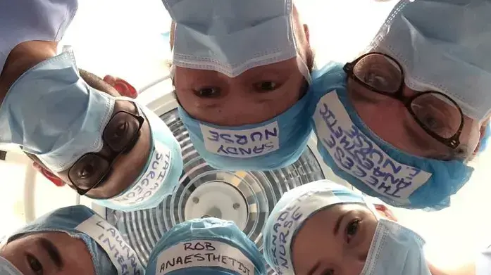 צוות חדר ניתוח עם כובעים שעליהם שמותיהם ותפקידיהם צוות חדר ניתוח עם כובעים שעליהם שמותיהם ותפקידיהם