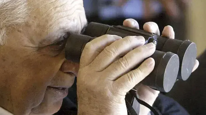 ראש ממשלת ישראל אריאל שרון מביט על תרגיל במתקן אדם באמצעות משקפת מכוסה - 2002
