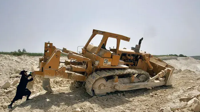 מפגין חרדי דוחף בולדוזר במהלך הפגנה נגד הריסת קברים תוך כדי בניית כביש שש סמוך לקיבוץ רגבים - אפריל 2005