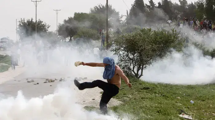 מפגין פלסטיני בועט במיכל גז מדמיע שנורה ע"י חייל מג"ב מפגין פלסטיני בועט במיכל גז מדמיע שנורה ע"י חייל מג"ב